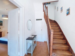 Una escalera con escalones de madera y barandilla, una puerta blanca, una pequeña mesa con un florero y un espejo fijado a la pared.