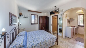 Quarto com cama, escrivaninha, guarda-roupa e um arco que dá para o banheiro.