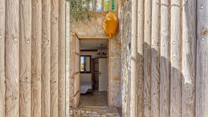 Uma porta de madeira dá acesso a um quarto com cama e piso de pedra.