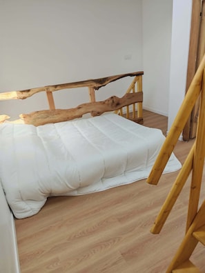 A room with a wooden bed frame, white bedding, and wooden flooring.