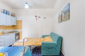 Ein kleiner, kompakter Raum mit Küchenzeile, einem Bett mit gemusterten Textilien, einem grünen Sofa und zwei an der Wand hängenden Bildern.