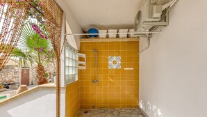 A bathroom with yellow tiles, a shower, and a fan on the wall. - Mono Glicine - Charming Studio on the Salento Coast (Salve)