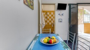 A room with a dining table, a fruit plate, a television, and a door leading to a bathroom. - Mono Glicine - Charming Studio on the Salento Coast (Salve)