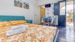 A bedroom with a bed, a TV, a door leading to a balcony, and a table with chairs. - Mono Glicine - Charming Studio on the Salento Coast (Salve)