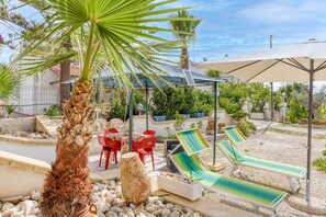 Un patio con sillones de descanso, una palmera y un espacio de estar cubierto.