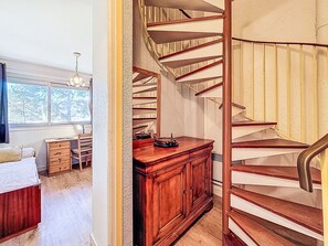 A bedroom with a wooden desk, a dresser, and a spiral staircase. - Plein Sud by Interhome (La Trinité Sur Mer)