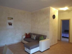 A living room with a sofa, a clock, and a framed picture on the wall. - Casa Roberta apartment 5 delux (Capoliveri isola d'Elba)