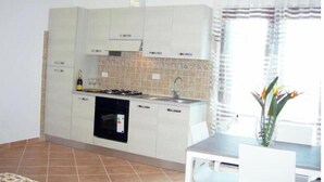 Une cuisine compacte avec des meubles blancs, une cuisinière à gaz, un évier et un coin repas comprenant une table et des chaises.