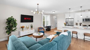 Un salón moderno con sofás color turquesa, una mesa de centro y un televisor que muestra 'NETFLIX'.