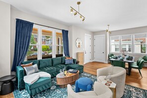 A modern living room with a green sofa, a round coffee table, and a dining area with green chairs. - 7BR Alexandria Retreat, Game Room + Pool Table, Near DC & Old Town (Alexandria)