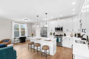 A modern kitchen with white cabinetry, stainless steel appliances, and a central island with stools. - 7BR Alexandria Retreat, Game Room + Pool Table, Near DC & Old Town (Alexandria)