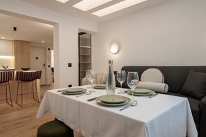 A dining area with a table set for four, a sofa, and a bar area with stools. - Bright & Stylish 2BR | Jacuzzi | Plaza Spain (Madrid)