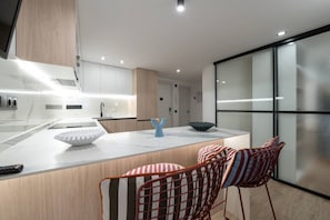 A modern kitchen with a marble countertop, a central island, and a seating area with striped chairs. - Bright & Stylish 2BR | Jacuzzi | Plaza Spain (Madrid)