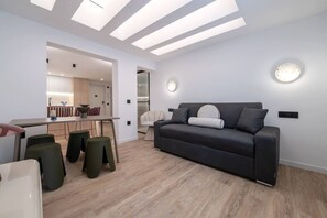 A modern living room with a sofa, a dining area, and a kitchen visible through an open doorway. - Bright & Stylish 2BR | Jacuzzi | Plaza Spain (Madrid)