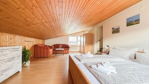 Ein modernes Hotelzimmer mit Holzboden, einer Couch, einem Bett mit karierter Bettwäsche, einem kleinen Tisch und einem Blumentopf.