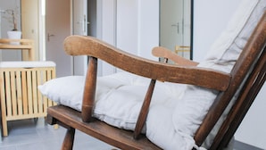 Ein hölzerner Stuhl mit weißen Kissen in einem Raum mit Holzboden und weißer Wand.