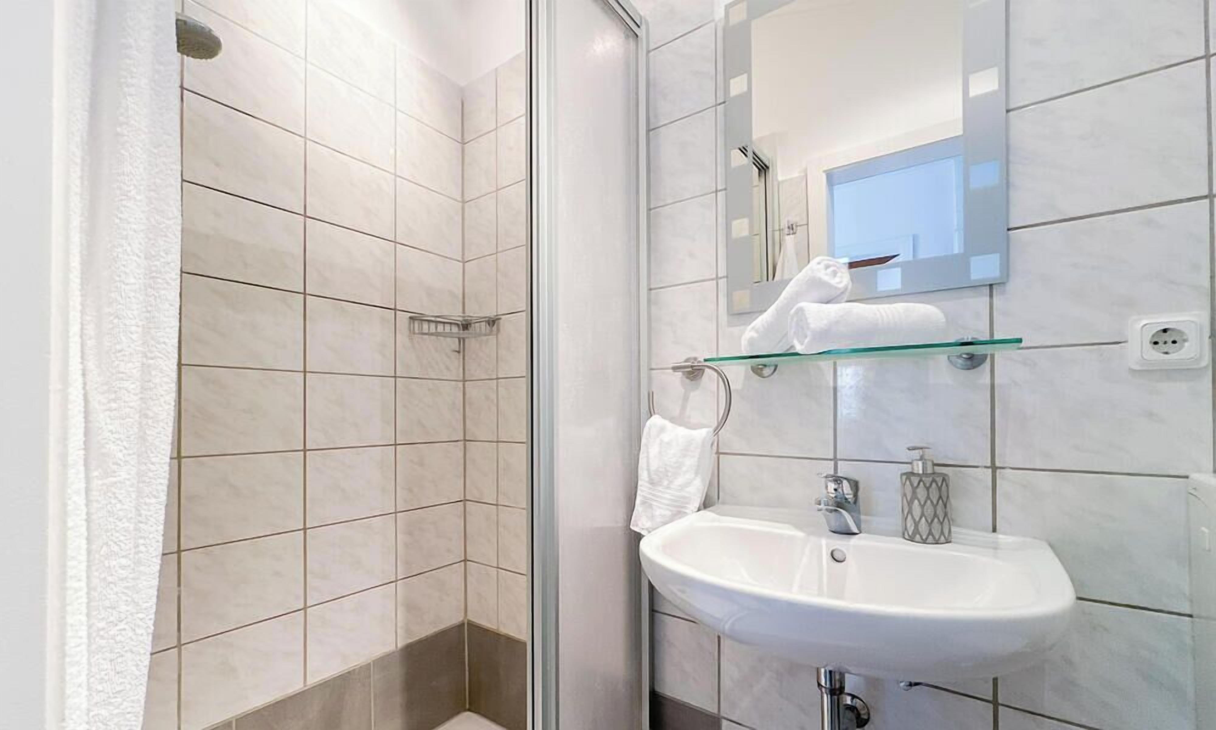 A modern bathroom with a glass shower enclosure, a white sink, and a mirror above the sink.