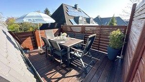 Eine Holzterrasse mit Tisch und Stühlen, einem Blumentopf und einem blauen Sonnenschirm.