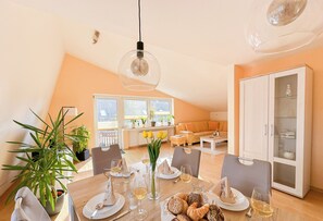 Uma sala de jantar com uma mesa posta para dois, um vaso com flores e um armário com portas de vidro.