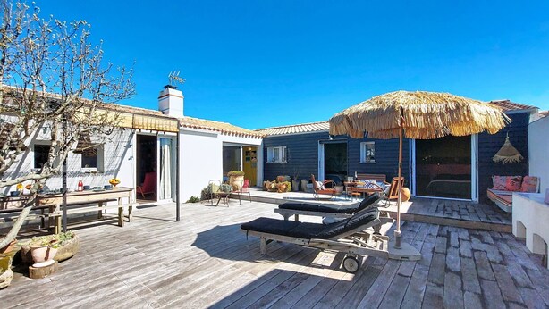 Een houten terras met een lounge stoel, een tafel en een rieten parasol.