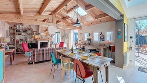 Een ruime keuken met houten balken, een eethoek met kleurrijke stoelen en een groot raam.