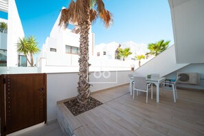 Eine Dachterrasse mit einer Palme, einem Tisch mit Stühlen und einer Klimaanlage.