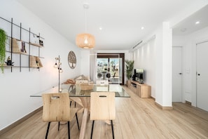 Ein modernes Wohnzimmer mit einem Glastisch, Holzstühlen, einem Fernseher und einem großen Fenster.