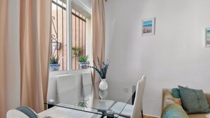 A modern living room with a glass dining table, white sofas, a beige sofa with a green throw, and a view of the outside through a window with curtains. - La Familia by Interhome (Los Alcázares)