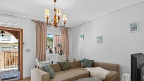 A living room with a beige sofa, a glass coffee table, a TV, and a chandelier. - La Familia by Interhome (Los Alcázares)