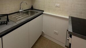Una cocina con armarios blancos, un fregadero, un ventanal con persianas y un salpicadero de azulejos.