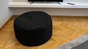 Una sala de estar moderna con un televisor de pantalla plana sobre un estante blanco, un reposapiés negro y un suelo de madera con estampado tipo espiga.
