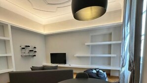 Una sala de estar moderna con una mesa redonda, sofás oscuros, un televisor de pantalla plana y estanterías empotradas.