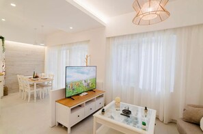 A modern living room with a flat-screen TV, a glass coffee table, a dining area with chairs, and large windows with sheer curtains. - Old Town Luxury Apartment with Private Terrace, Wi-Fi and Air Conditioning (Kos)