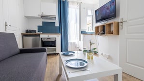 Een moderne keuken met een flatscreen televisie, een eettafel met borden en bestek, een bank en een kleine plant.