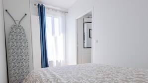 Een slaapkamer met een bed, een kast, een spiegel en een raam met gordijnen.
