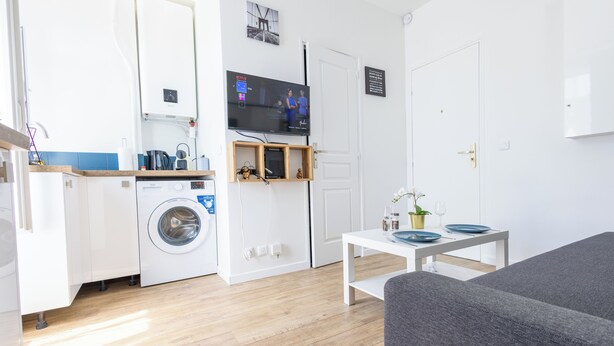 Een knus woongedeelte met een wasmachine, een televisie, een eettafel en een bank.