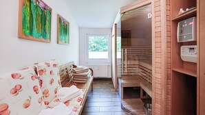 Käytävä, jossa on puinen penkki, sauna ja ikkuna, josta avautuu näkymä vehreään maisemaan.