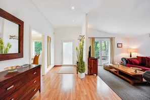 Ein geräumiger Wohnbereich mit Holzboden, einem roten Sofa, einem Holztisch, einer TV-Konsole und einem großen Spiegel.