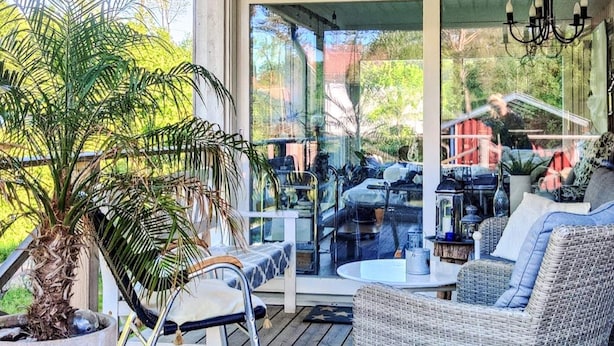 A covered outdoor seating area with wicker furniture, a potted plant, and a glass door leading to a patio. - 4 Star Holiday Home in Karna (Kärna)