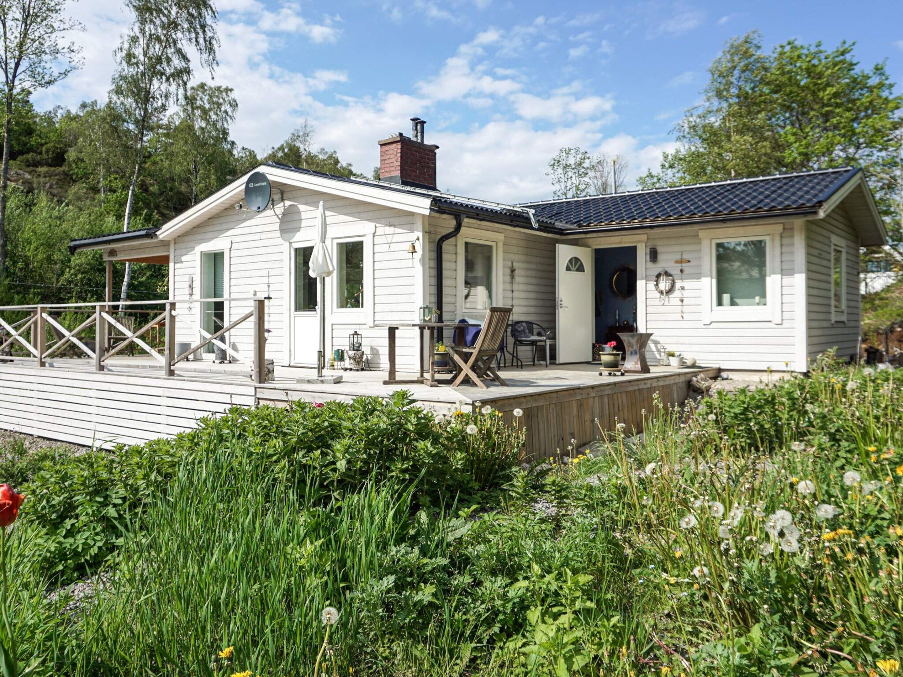 A white cabin with a deck, surrounded by greenery.