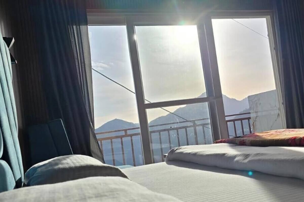 A bedroom with a bed, a window with a view of mountains, and curtains.