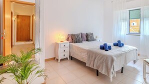 Une chambre à coucher avec un lit, une table de chevet, une lampe et une fenêtre avec des rideaux.