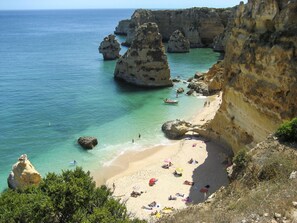 A coastal beach with clear turquoise waters, rocky formations, and a sandy shore with people and umbrellas. - Ninho do Mar by Interhome (Armação de Pêra)