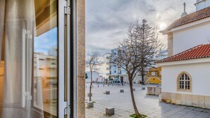 Une vue depuis une fenêtre donnant sur une cour intérieure, avec un sol carrelé, un arbre et des bâtiments à la façade jaune.