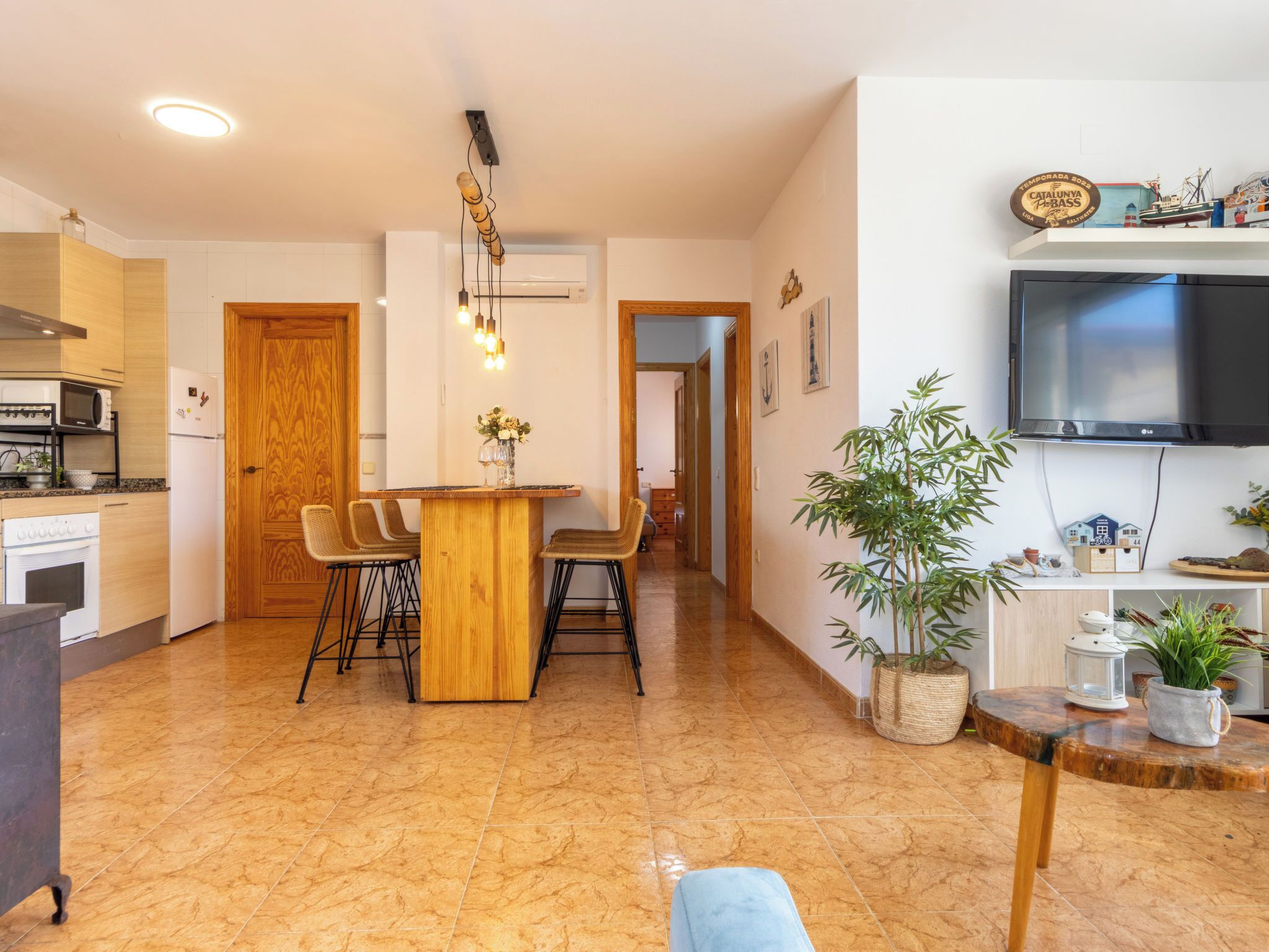 A modern kitchen with a dining area, a TV mounted on the wall, and a wooden door.