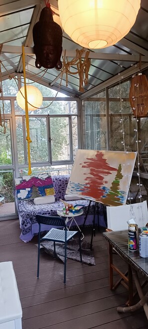 A conservatory with a painting on easel, a sofa, and a table with art supplies. - House by the sea (Agios Dimitrios)
