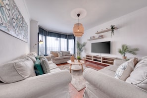 Ein modernes Wohnzimmer mit einer Sofagarnitur, einem Couchtisch, einem Fernseher und dekorativen Pflanzen.