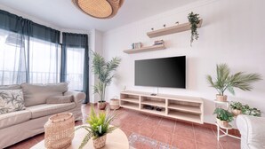Un salon avec un canapé, une télévision, des étagères et des plantes.