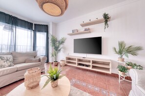 Een woonkamer met een bank, televisie, planken en planten.