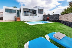 Ein modernes Haus mit Swimmingpool, Steinmauer und Rasenfläche.